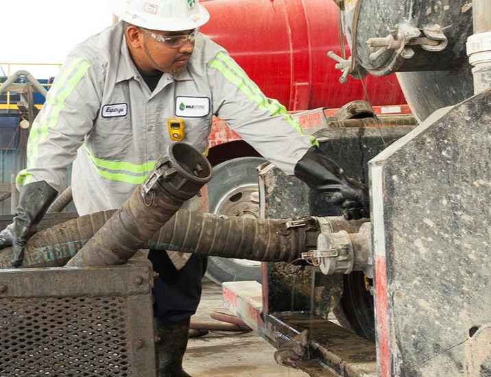 A Milestone worker attaching a pump to an oilfield waste vehicle.